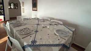 Comedor con una mesa redonda dispuesta para seis comensales, sillas blancas y mantel blanco con diseños azules.