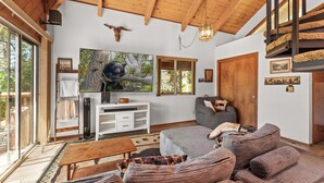 A cozy living room with a large sofa, a coffee table, and a fireplace. There is a painting of a bear on the wall and a wooden ceiling.