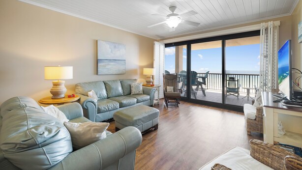 A spacious living room with a large window, a ceiling fan, and a view of the ocean. - Romar House 404A by Liquid Life (Orange Beach)