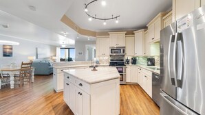 A modern kitchen with a central island, stainless steel appliances, and a dining area with a sofa and chairs. - Romar House 404A by Liquid Life (Orange Beach)