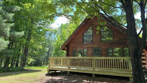A wooden cabin with a deck, surrounded by trees.