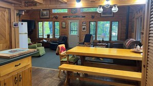 A cozy cabin interior with a wooden dining table, benches, a refrigerator, and a fireplace.