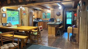 A cozy cabin-style kitchen with wooden floors, a dining area with a table and chairs, and a bar area with stools.