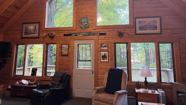 A log cabin interior with a high ceiling, large windows, and a cozy seating area.