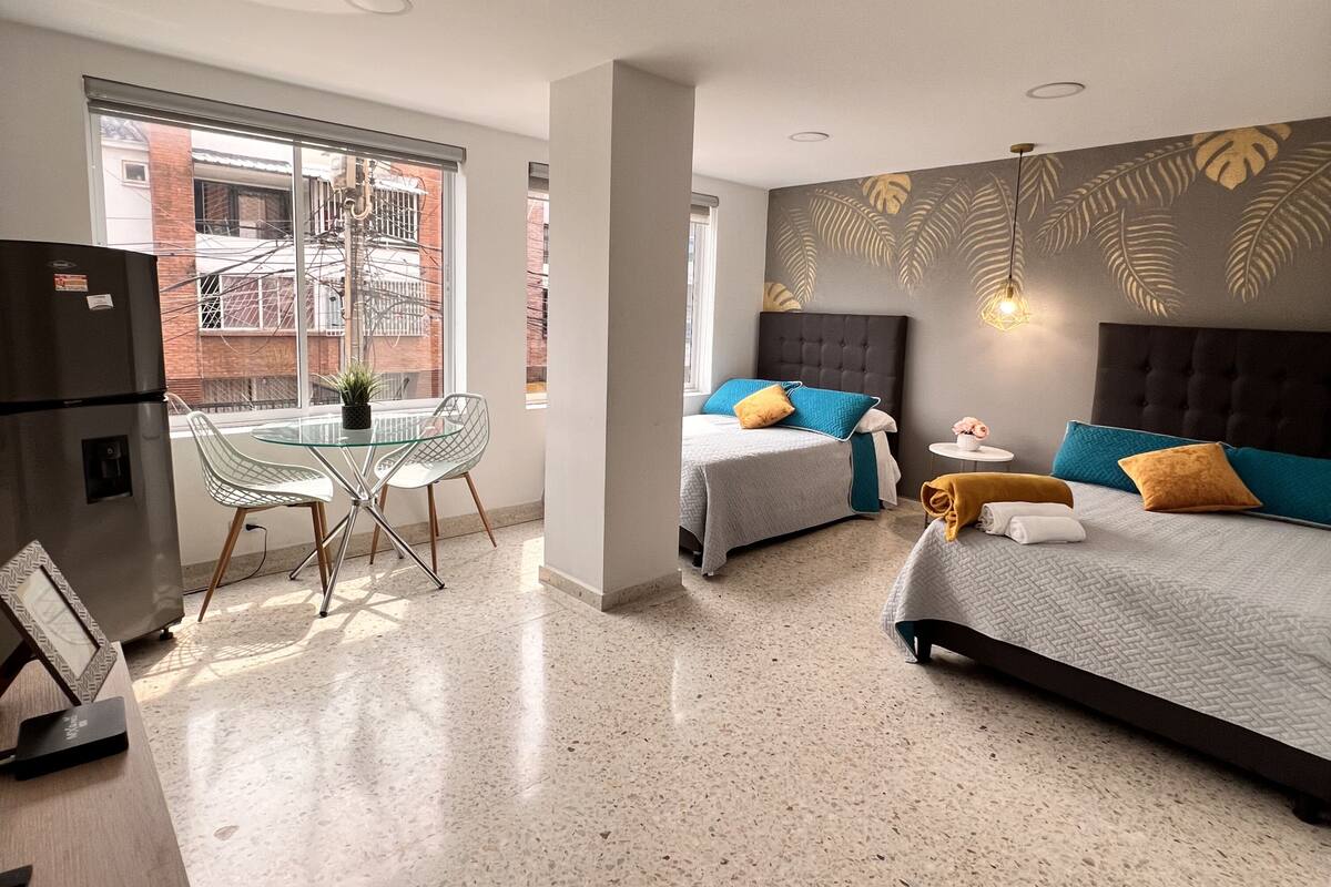 Une chambre d’hôtel moderne avec une table à manger en verre, deux lits, un réfrigérateur et une vue sur l’extérieur.