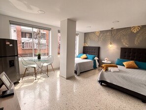 A modern hotel room with a glass dining table, two beds, a refrigerator, and a view of the outside. - Park 66 Apartaestudios (Cali)