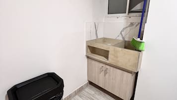 A small bathroom with a toilet, a sink, a mirror, and a broom leaning against the wall.