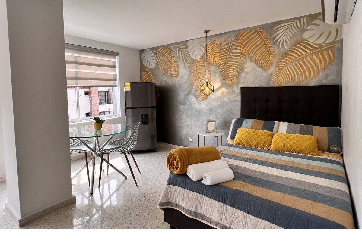 Une chambre d’hôtel avec un lit, une petite table, une chaise, un réfrigérateur et une fenêtre avec des stores.