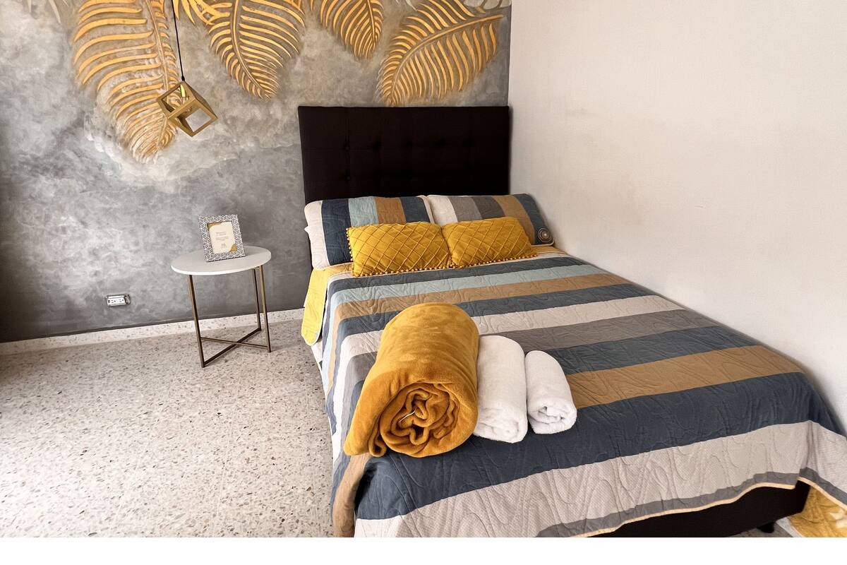 Une chambre à coucher comprenant un lit, une table de chevet, un luminaire fixé au mur et une prise de courant.