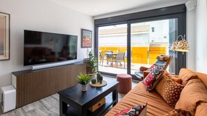 A modern living room with a flat-screen TV, a wooden console table with plants, a sofa with patterned cushions, and a sliding glass door leading to an outdoor dining area. - Penthouse Morning Star by Fidalsa (Torrevieja)