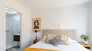 A modern bedroom with a large bed, a headboard, a bedside table with a lamp, a framed picture on the wall, and a potted plant. - Penthouse Morning Star by Fidalsa (Torrevieja)