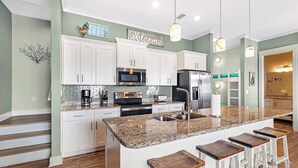 A modern kitchen with white cabinets, granite countertops, and a central island with bar stools. - Little Lagoon Cottage for 8 - Free Activities (Gulf Shores)