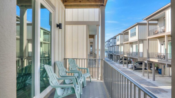 A balcony with chairs, a railing, and a view of adjacent buildings. - Little Lagoon Cottage for 8 - Free Activities (Gulf Shores)