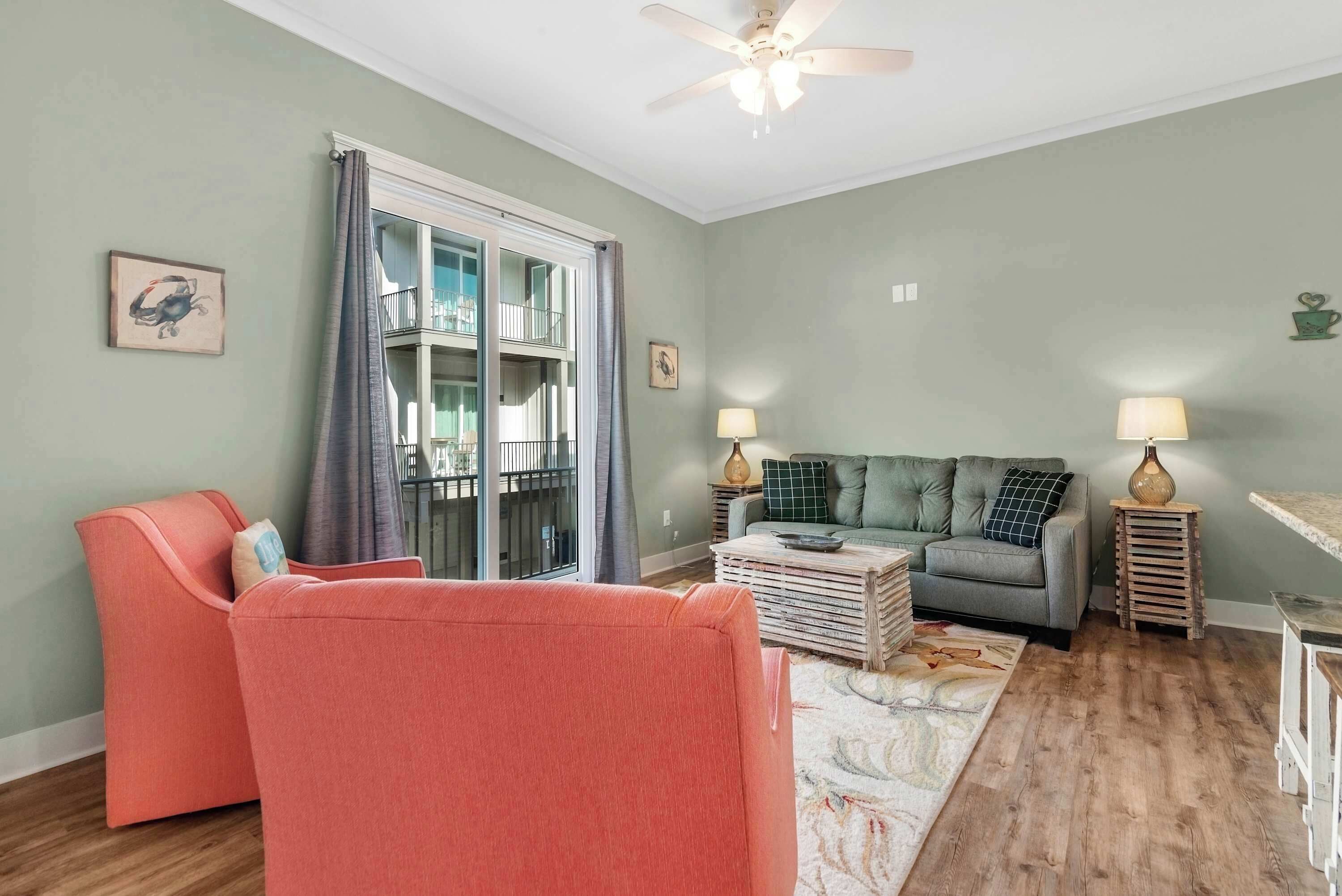 A living room with a grey sofa, a pink armchair, a wooden coffee table, and a ceiling fan.