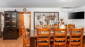 A dining area with a wooden table and chairs, a cabinet with glassware, a world map mural, and a flat-screen TV mounted on the wall.