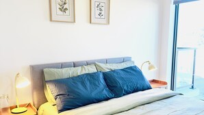 A bedroom with a bed, bedside tables, a lamp, and framed botanical prints on the wall.