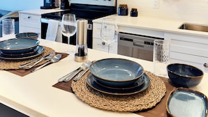 A modern kitchen with white cabinetry, a built-in microwave, and a stove. There are two dining tables set with plates, cutlery, and glasses.