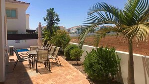 Eine Terrasse mit Tisch und Stühlen, ein Pool und Blick auf benachbarte Häuser.
