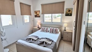 Ein Schlafzimmer mit einem Bett, zwei Nachttischen, einem Ventilator und einem Fenster mit Blick.