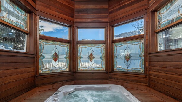 A wooden cabin with a hot tub, large windows with stained glass, and a view of mountains. - Smuggler Mine — Modern Pet-Friendly Retreat Near Slopes (Telluride)