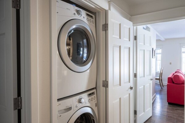 A laundry room with a front-loading washer and dryer, white doors, and a red chair in the background.