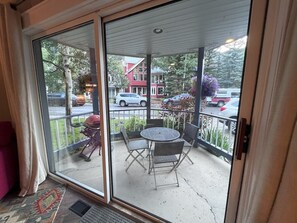 A sliding glass door leading to an outdoor patio with a round table and chairs, a red building in the background, and a parked car.