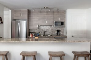 A modern kitchen with stainless steel appliances, a tiled backsplash, and a bar area with stools.