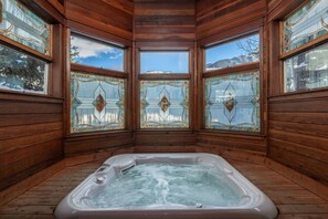 A wooden cabin with a hot tub in the center, large windows with stained glass, and a view of a snowy landscape. - Smuggler Mine — Pet-Friendly Condo in Telluride (Telluride)