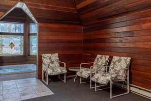 A cozy corner with wooden walls, a hot tub, and two chairs with a leaf pattern.