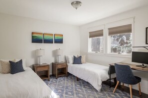 A hotel room with two beds, a desk with a computer, and a window with a view of trees.