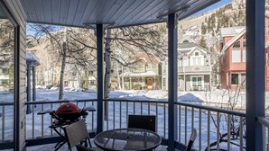 Un espace extérieur abrité, équipé d’une table et de chaises, d’un barbecue, et offrant une vue sur les maisons et les arbres en arrière-plan.