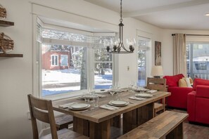 A dining area with a wooden table set for four, large windows, and a red sofa.