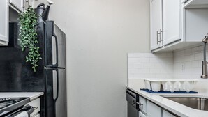 A compact kitchen with white cabinets, a black refrigerator, and a wooden floor. - Hyde Park Escape (Austin)