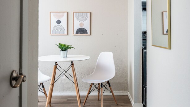 A modern dining area with a round table, two white chairs, a potted plant, and two framed artworks on the wall. - Hyde Park Escape (Austin)