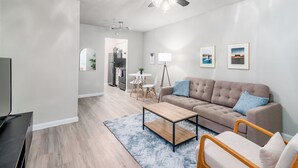A modern living room with a sofa, coffee table, and TV. There is a ceiling fan and a dining area in the background. - Hyde Park Escape (Austin)