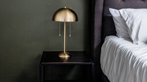 A neatly made bed with white linens, a dark upholstered headboard, and a small bedside table with a gold lamp. - Hyde Park Escape (Austin)