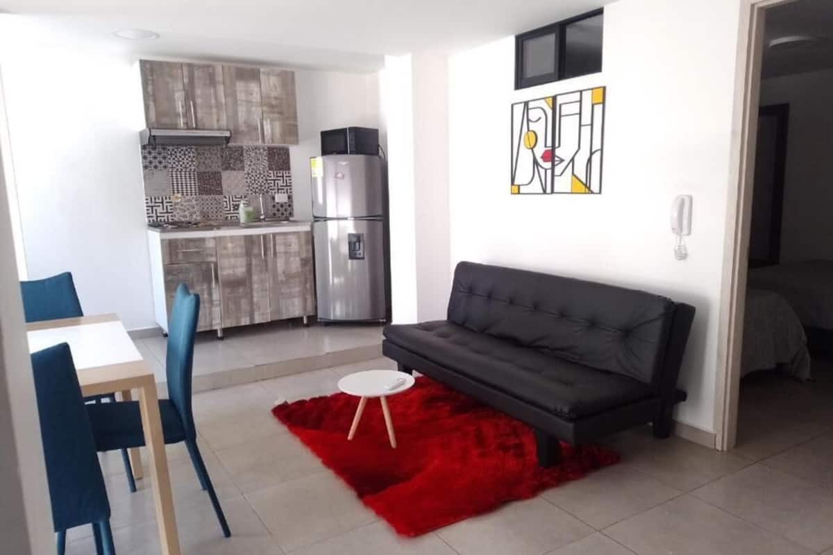A modern living room with a grey sofa, a red rug, and a dining area with blue chairs.