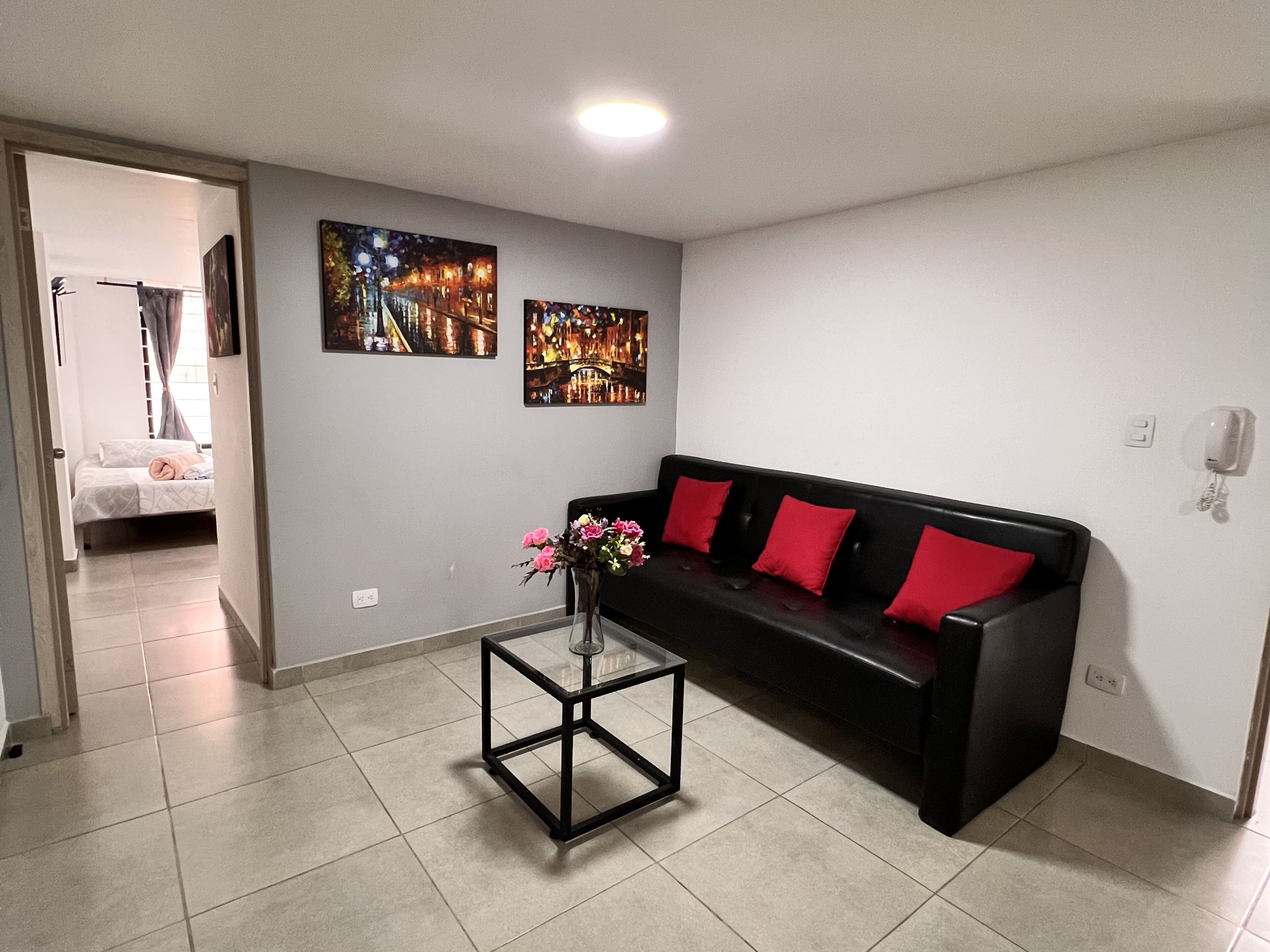 A modern living room with a black sofa, red cushions, a glass coffee table, and two wall-mounted paintings.
