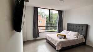 A bedroom with a bed, a window, and a television mounted on the wall. - Park 2009 Apartaestudios (Cali)