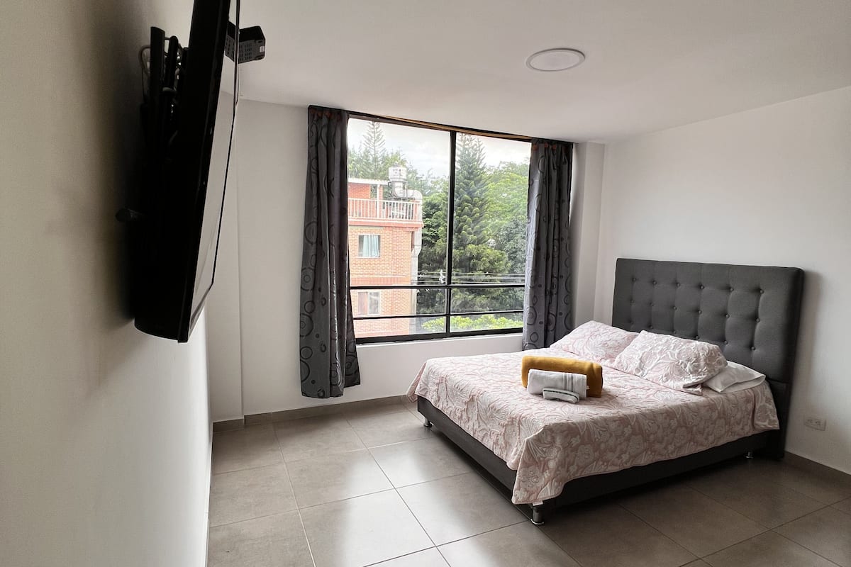 A bedroom with a bed, a window, and a television mounted on the wall.