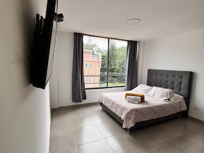 A bedroom with a bed, a window, and a television mounted on the wall. - Park 2009 Apartaestudios (Cali)