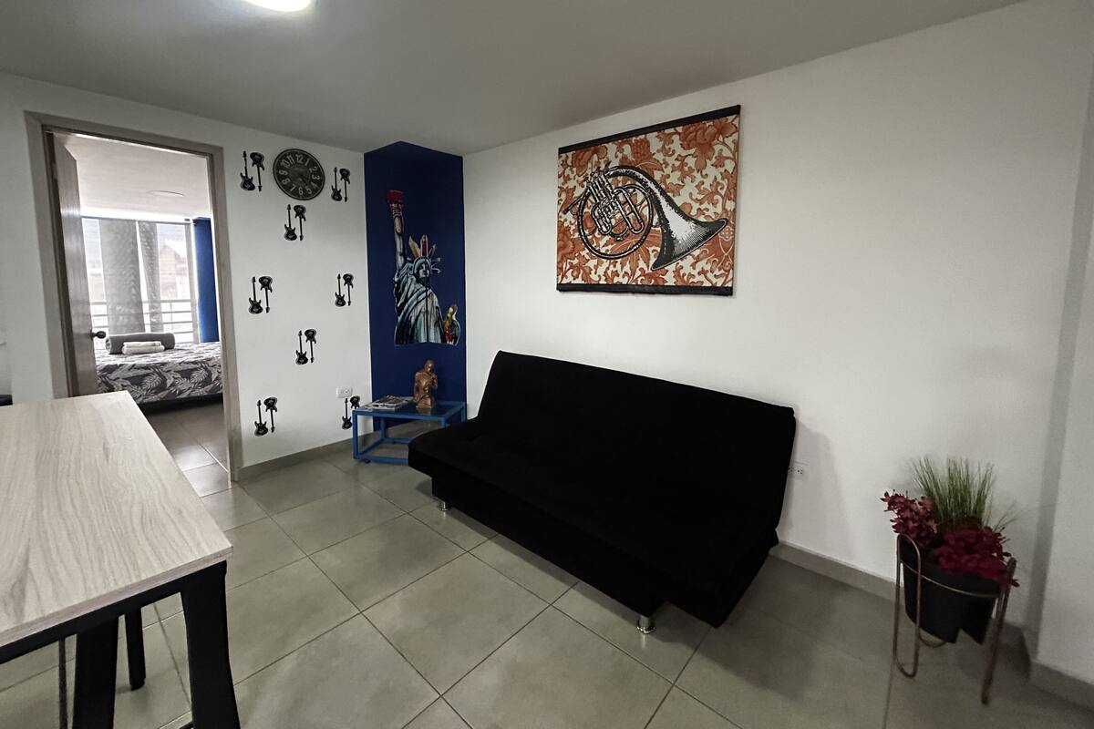 A living room with a sofa, a dining table, a blue accent wall, a wall clock, and a decorative statue.