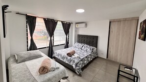 A bedroom with two beds, a window with curtains, an air conditioner, and a small table. - Park 2009 Apartaestudios (Cali)