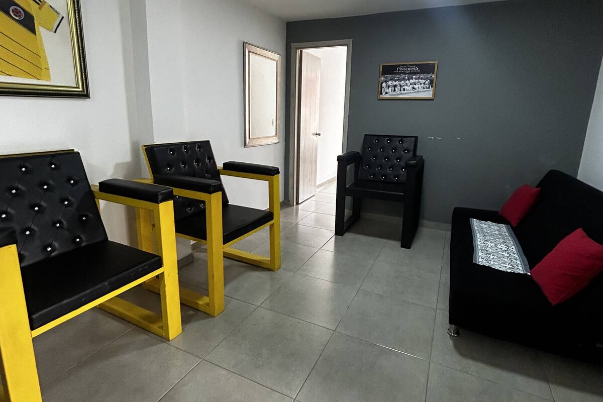A room with a black sofa, two yellow chairs, a framed picture, and a door.
