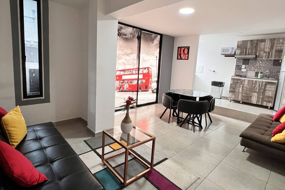 A modern living room with a sofa, a coffee table, a dining table with chairs, and a kitchen area.