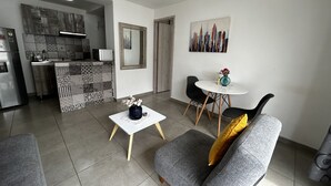 A modern living space with a kitchen, dining area, and a gray sofa with a yellow pillow. - Park 2009 Apartaestudios (Cali)