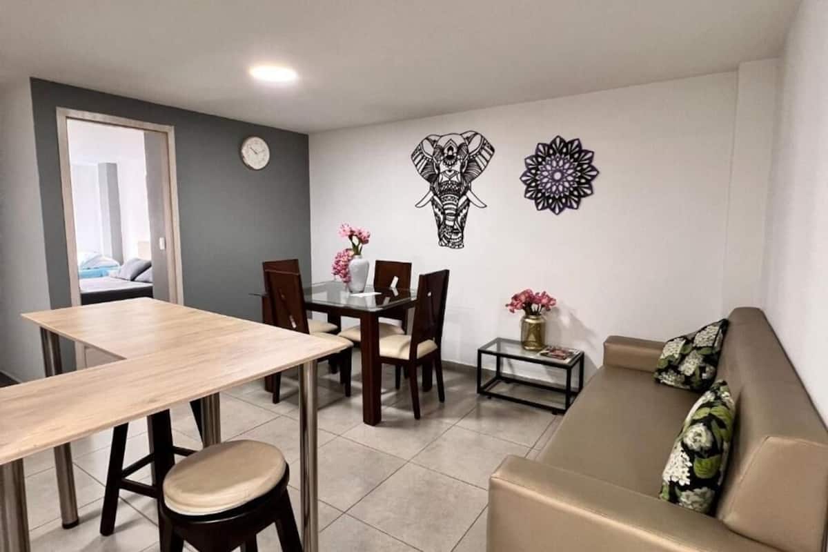 A dining area with a table and chairs, a sofa, and decorative wall art.