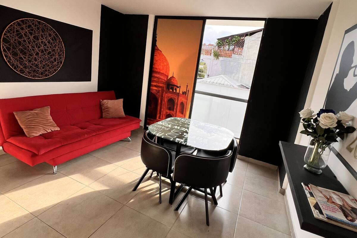 A modern living room with a red sofa, a round table with chairs, and a large window with a view of a building.