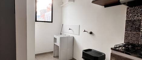 A compact kitchen with a microwave, a gas stove, a trash bin, and a window.