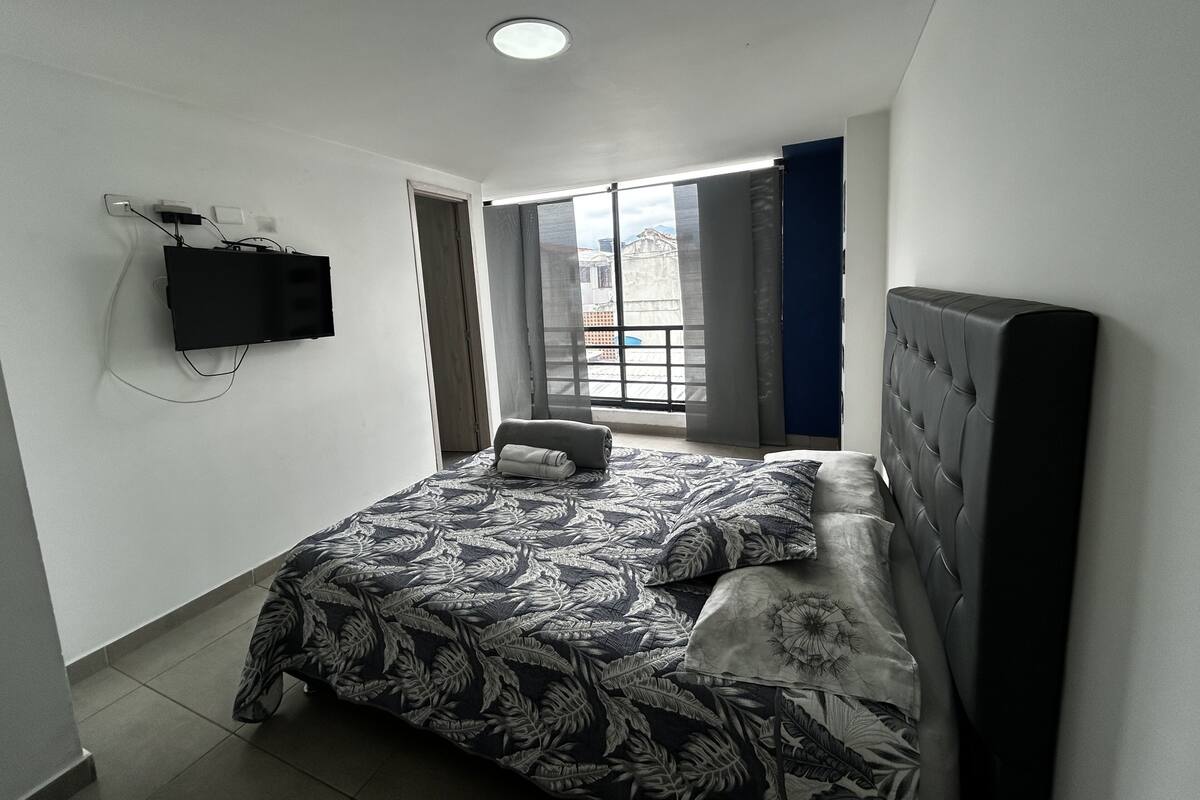 A bedroom with a bed, a television mounted on the wall, and a window with curtains.